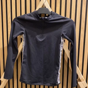 Svart långärmad tröja från Aim'n - Snygg svart långärmad tröja från Aim'n med dragkedja framtill och logotyp längs sidorna. Tillverkad i polyester och spandex för en bekväm passform. Perfekt för träning eller en sportig look.