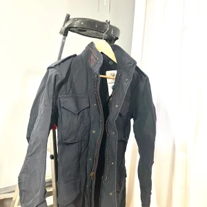 Marinblå M90 jacka från Alpha Industries - Säljer en marinblå M90 jacka från Alpha Industries med dragkedja och flera praktiska fickor och huva! Jackan har långa ärmar och en klassisk militärdesign M90 som passar perfekt för höst och vår. Passar kille eller tjej 175-178 cm med smal midja, som en MC jacka runt revbenen! Sjukt snygg! M för tjej.