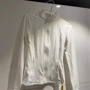 Vit tränings jacka från Glowmode - Säljer en stilren vit jacka från Glowmode med dragkedja framtill och praktiska fickor. Perfekt för en sportig look eller en avslappnad dag. Jackan har långa ärmar och en hög krage för extra komfort.