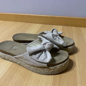Beige sandaler med rosett - Snygga beige sandaler med en dekorativ rosett på ovansidan. Sandalerna har en platåsula i flätad stil som ger en somrig känsla. Perfekta för varma dagar.