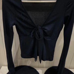 Marinblå långärmad topp från Gina Tricot - Snygg marinblå långärmad topp från Gina Tricot i storlek XS. Toppen har en knytning framtill och en djup v-ringning som ger en stilren look. Perfekt för att lyfta din outfit!