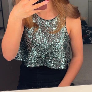 Glittrig ärmlös topp - Snygg glittrig topp i blå med ärmlös design. Perfekt för festliga tillfällen med en croppad passform som ger en trendig look.