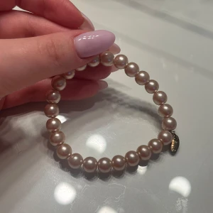 pärlarmband med rosefärgade pärlor - Elegant pärlarmband med ljusrosa pärlor och en liten berlock. Ett väldigt unikt armband, använt någon gång. 