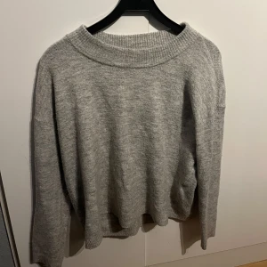 Grå stickad tröja från Vero Moda - Mysig grå stickad tröja från Vero Moda. Perfekt för kyliga dagar med sin bekväma passform och ribbade detaljer vid halsen. Ett stilrent val för garderoben.