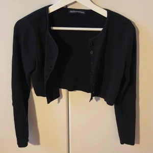Svart croppad kofta  - Svart stickad croppad kofta från Brandy Melville med knappar framtill. Bra skick. Small.