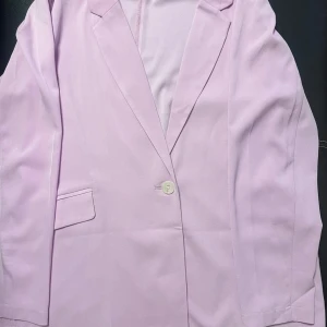 Ljuslila kavaj från Amisu/ new yorker - Snygg ljuslila kavaj från Amisu med klassisk design. Kavajen har en enkel knapp framtill och två fickor. Perfekt för att ge en färgklick till din outfit.