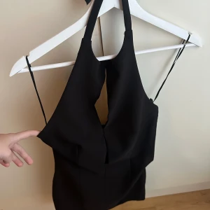 Svart klänning - Elegant svart klänning med glittrig rosett & halterneck-design. Öppning vid bröstet! Endast använd en gång. Storlek XS.