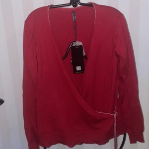 Röd omlottkofta från Freequent - Snygg röd omlottkofta från Freequent med långa ärmar och knytband i midjan. Perfekt för att lägga till en färgklick i garderoben. Koftan har en mjuk och bekväm passform.