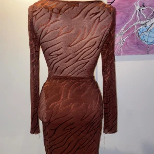 Brun mönstrad klänning med cut-outs - Trendig brun klänning med zebramönster och stiliga cut-outs framtill. Klänningen har långärmade ärmar och en tight passform som framhäver figuren. Knapparna där fram är formade som hjärtan. Priserna går att diskutera!! 