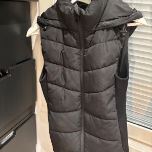 Svart dunväst med huva - Snygg svart dunväst med dragkedja och huva från Zara. Perfekt för kyliga dagar när du vill hålla värmen utan att kompromissa med stilen.