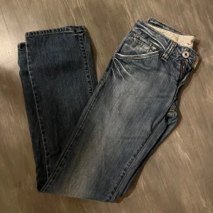 Blå jeans med knappdetalj - Snygga blå jeans med en klassisk femficksdesign och knappdetalj vid fickan. Jeansen har en lätt tvättad look och är perfekta för en avslappnad stil. ( inte skinny som det ser ut på bilden ) 