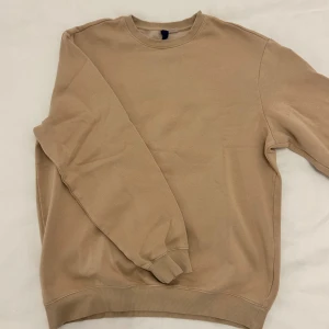 Beige sweatshirt från Gildan - Säljer en stilren beige sweatshirt från H&M. Tröjan har en klassisk rund halsringning och långa ärmar med ribbade muddar. Perfekt för en avslappnad look. Storleken på sweatshirten är en M. Inga fläckar eller slitage. Skriv gärna om ni har frågor allt ifrån pris till fler bilder. 