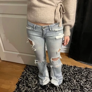 Ljusblåa slitna lågmidjade jeans - Säljer mina sjuuuukt snygga ljusa jeans med slitningar och hål för en trendig look. De är bootcut längst ner och är väldigt lågmidjade. Tycker de är sååå snygga men behöver sälja då de inte passade mig. Min kompis på bilden är ca 161cm och är långa på henne. Säljer för 850kr men pris går alltid att diskutera vid snabb affär🥰