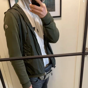 Moncler Jacka - Snygg grön jacka från Moncler med dragkedja och huva. Jackan har långa ärmar och en stilren design med Moncler-logga på ärmen. Perfekt för en casual look. Passar både M & L
