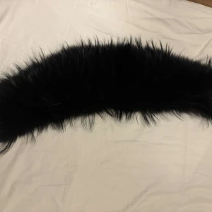 Svart pälsdetalj - Säljer en elegant svart pälsdetalj i äkta päls. Perfekt för att ge din jacka eller kappa en lyxig touch. Pälsen är mjuk och fluffig, vilket ger en stilren look. Endast kemtvätt rekommenderas för att bevara kvaliteten. Priset kan även diskuteras 😊