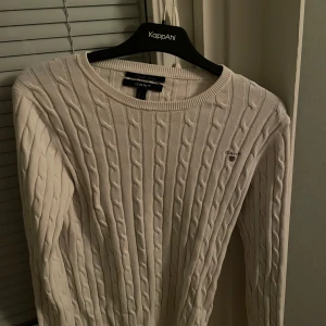 Vit kabelstickad tröja från GANT - Säljer en stilren vit kabelstickad tröja från GANT i stretchig bomull. Tröjan har en klassisk rund hals och långa ärmar, perfekt för kyligare dagar. En tidlös garderobsklassiker! Orginal priste 600