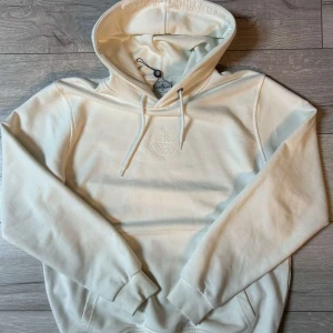 Vit hoodie från Stone Island - Säljer en stilren vit hoodie från Stone Island med broderad logga på bröstet och justerbar huva. Perfekt för en avslappnad look. Skriv på dm för mer frågor. Pris kan sänkas