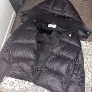 Svart pufferjacka från Calvin Klein Jeans - Hej säljer en Snygg svart pufferjacka från Calvin Klein med luva och dragkedja.Vid intresse skriv t mig!