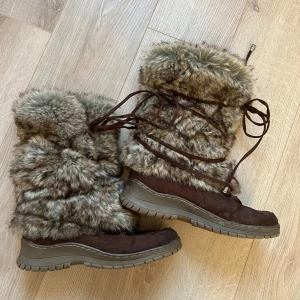 Bruna vinterstövlar med fuskpäls - Säljer ett par bruna vinterstövlar med fuskpäls och snörning. De har en robust sula och är fodrade för extra värme. Perfekta för kalla vinterdagar.