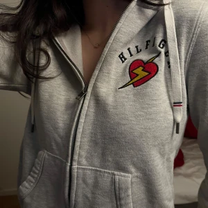 Tommy Hilfiger hoodie  - Så söt grå zipup från Tommy Hilfiger med dragkedja. Storleken är S men passar XXS-S💕 Har nu blivit lite nopprig o har ett svagt mörkare parti på ena armen (se bild) men utöver det toppen
