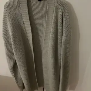 Mysig grå stickad kofta med lång ärm och öppen design. Perfekt för kyliga dagar och att mysa i hemma. Enkel och stilren, passar till det mesta i garderoben.