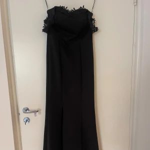 Svart klänning med broderade axelband - Svart klänning med broderade axelband och slits. Fotlång 