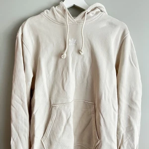 Beige hoodie från Adidas - Säljer en supermysig beige hoodie från Adidas. Den har en klassisk känguruficka och justerbar huva med dragsko. Mycket bra skick förutom en defekt på tröja (se bild på fläck)