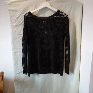 Svart stickad tröja med hålmönster - Säljer en cool svart stickad tröja med ett unikt hålmönster. Perfekt för lager-på-lager-stil eller som statement-plagg. Tröjan har långa ärmar och är superbekväm att ha på sig. Passar perfekt till både vardag och fest!