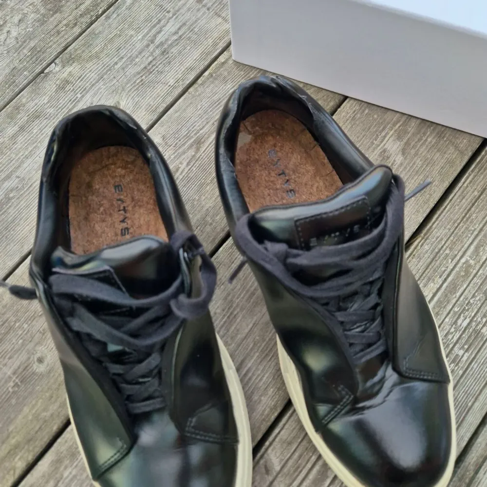 Säljer ett par Eytys Doja Leather black skor i gott skick Stl 43 Robusta low-top sneakers i glänsande svart läder. Har en förhöjd tåhätta, anpassade Eytys gummisulor och dold öppning. Med fotvalvsstöd och korkinnersulor för maximal komfort. . Skor.