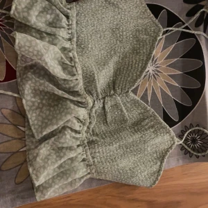 Grön ribbad topp med volangdetaljer - Söt grön ribbad topp med volangdetaljer och smala axelband från Gina Tricot. Perfekt för en somrig look med sitt lätta och luftiga material. Toppen har en smockad design som ger en bekväm passform.