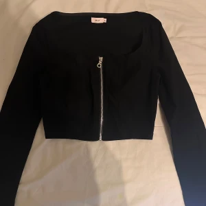 Svart croppad topp med dragkedja - Snygg svart croppad topp från Nelly med dragkedja framtill. Toppen har långa ärmar och en stilren design som passar perfekt till olika outfits. Storlek 36