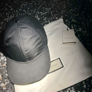 GUCCI KEPS NYLON - Snygg svart keps från Gucci med diskret mönster och nätpaneler för ventilation. Perfekt för en stilren look. Kepsen har en justerbar rem för optimal passform. Skicket är bra på den men lite använd.  En knap på baksidan är av,Mycket svår o rare keps att få tag på/ storlek L