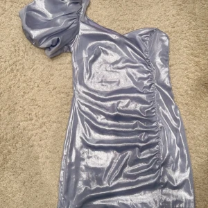 Glittrig oneshoulder klänning från & Other Stories - Snygg glittrig oneshoulder klänning i silver från & Other Stories. Perfekt för en kväll ute med sin skimrande look och unika design. Klänningen har en kort längd och en elegant rynkad detalj på sidan. Ett måste för garderoben! ✨