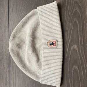 Parajumper mössa - Snygg grå mössa från Parajumpers med ribbad design och ett broderat märke framtill. Perfekt för kyliga dagar och ger en stilren look. Tillverkad i mjukt material för extra komfort. Nypris 700-800.
