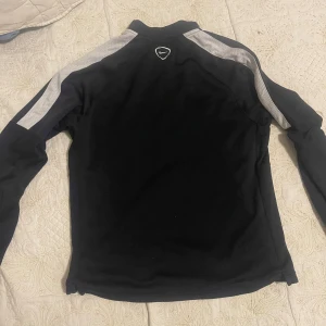 Svart tränings tröja från Nike - Säljer en svart långärmad tränings tröja från Nike med vita detaljer. Tröjan har en dragkedja framtill gråa paneler på axlarna. Perfekt för träning eller vardagsbruk. I bra skick är det, storlek 147-158 cm för 12-13 årig barn. L i barnstorlek. 