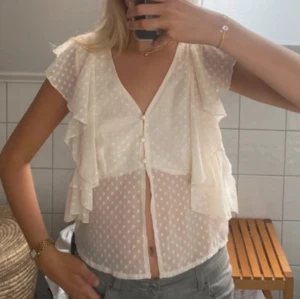 Vit blus med volanger - Säljer en söt vit blus med prickigt mönster och volanger. Blusen har korta ärmar och knappar framtill. Går inte att köpa längre!! Är i storlek M men passar även mig som brukar bära S💖💖