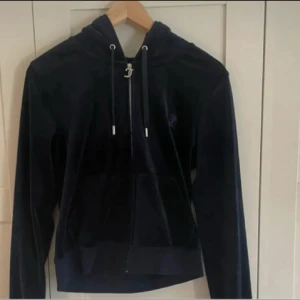 Mörkblå hoodie från Juicy Couture - Säljer en snygg mörkblå hoodie från Juicy Couture i mjukt sammetstyg. Tröjan har dragkedja framtill och en justerbar huva med snören. Perfekt för en avslappnad stil.
