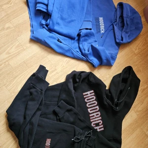 Hoodies från Hoodrich i blått och svart - Säljer två snygga hoodies från Hoodrich. En i blått med vit text och en i svart med röd text. Båda har en klassisk hoodie-design med långa ärmar och justerbar huva. Perfekta för en avslappnad stil.