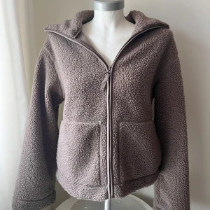 Brun teddyjacka med dragkedja - Mysig brun teddyjacka med dragkedja och huva. Perfekt för kyliga dagar med sina stora fickor och mjuka material. Jackan har en avslappnad passform och långa ärmar. Som ny 🥰Använd fåtal gånger. 