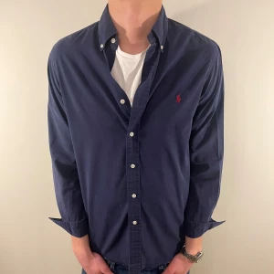 Mörkblå Ralph Lauren skjorta - Nu säljer vi ännu en fet polo skjorta som passar alla tillställningar! OBS skjortan har ett litet hål i ärmen som syns på sista bilden(vi sänker priset mycket pga detta) Du ska kunna uttrycka stil utan att det kostar för mycket!🕺🍾💼🤩  Storlek👔: M Nypris💰: ca 1499 kr