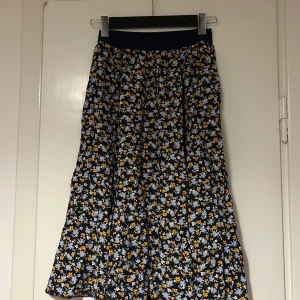 Blommig kjol från Arket  - Charmig blommig kjol från Arket i mörkblått med vita och gula blommor. Kjolen har en elastisk midja för bekväm passform. Inköpt för ca 699! 