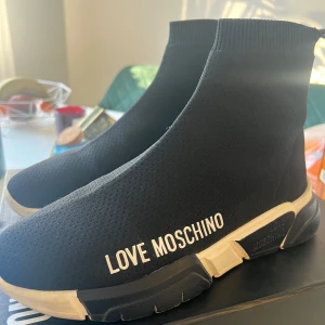 Svarta sneakers från Love Moschino - Snygga svarta sneakers från Love Moschino med en stilren design. Skorna har en elastisk överdel som ger en tight passform och en vit sula med märkets logga på sidan. Perfekta för en trendig look.