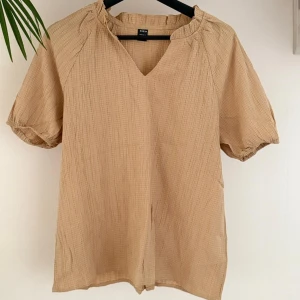 Beige blus, Shein - Beige blus från Shein med korta ärmar och v-ringning. Blusen har en lätt textur.