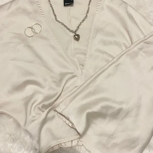 kräm vit omlottopp från Gina Tricot🤍 - Säljer en elegant kräm vit omlottopp från Gina Tricot. Toppen har en v-ringning och är kort. Är tillverkad i ett glansigt material som ger en lyxig känsla. Perfekt för att klä upp en outfit med stil. 💫