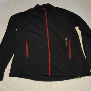 Svart fleecejacka från Didriksons - Säljer en svart fleecejacka från Didriksons med röd dragkedja och två fickor framtill. Jackan har långa ärmar och är perfekt för kyligare dagar. Den är en del av deras Thermal System, vilket gör den extra varm och skön. Perfekt för höst och vår!