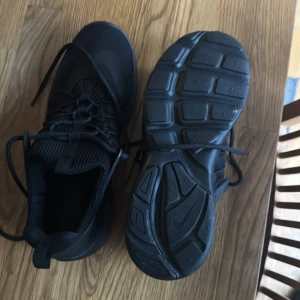 Svarta Nike sneakers - Snygga svarta Nike sneakers med en stilren design och snörning. Perfekta för en sportig look och bekväma för vardagsbruk. Sulan har ett bra grepp och ovandelen är i ett andningsbart material.