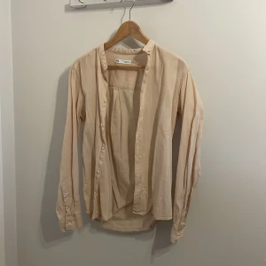 Beige skjorta från Zara - Säljer en stilren beige skjorta från Zara med långa ärmar och knappar framtill. Skjortan har en avslappnad passform och är tillverkad i ett lätt och bekvämt material. Perfekt för en casual look. Använd 1 gång på fest! Passar bra till sommaren! 