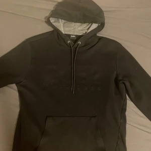 Hugo boss hoodie - Snygg svart hoodie från Hugo boss med diskret logga på bröstet. Den har en justerbar huva med dragsko och en praktisk magficka. Perfekt för en avslappnad stil. Pris kan diskuteras vid snabb affär skriv om ni undrar något