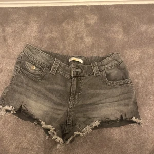 Grå jeansshorts från Gina Tricot - Snygga grå jeansshorts från Gina Tricot med fransiga kanter . Shortsen har en knapp och dragkedja framtill samt dekorativa knappar på bakfickorna. Perfekta för en avslappnad stil. Och super fina till sommaren