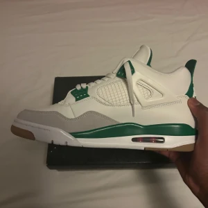 Nike Air Jordans SB - Snygga Nike Air Jordans i vitt med gröna detaljer. Skorna har en klassisk design med snörning och en bekväm sula. Perfekta för dig som vill ha en stilren look med en touch av färg.